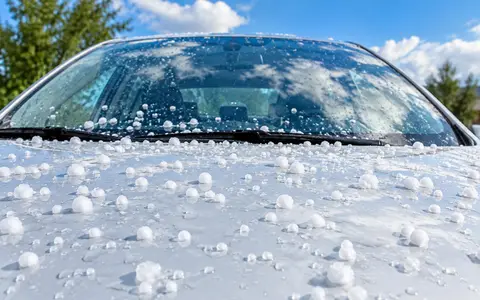 Capot y parabrisas de un auto cubiertos de granizo bajo un cielo que se despeja